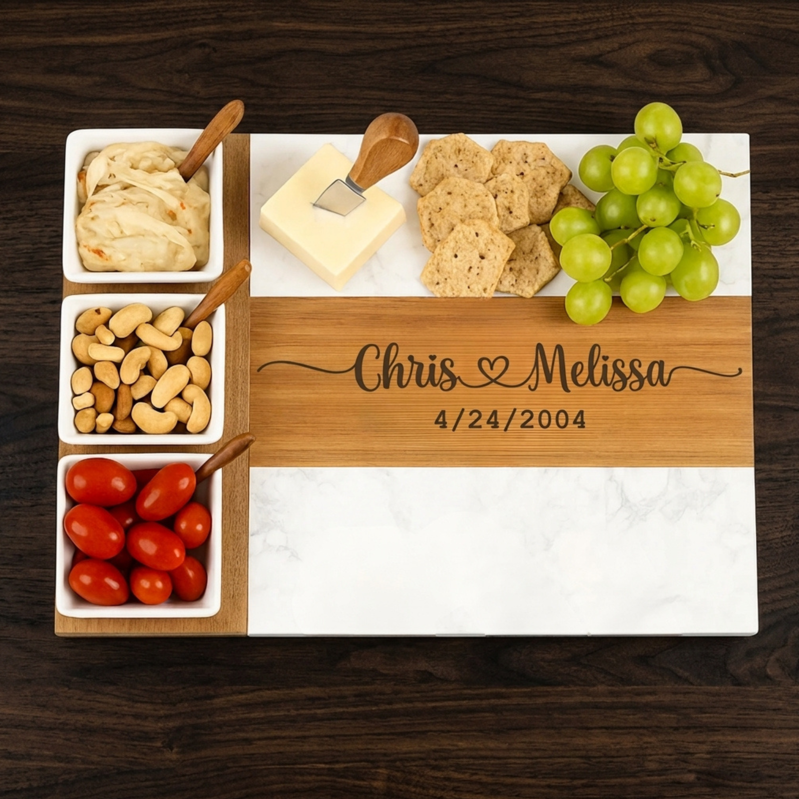 Wooden charcuterie board with ceramic bowls containing nuts, crackers, red tomatoes, cheese, wooden spreader, and engraved sample "Chris & Melissa 4/24/2004