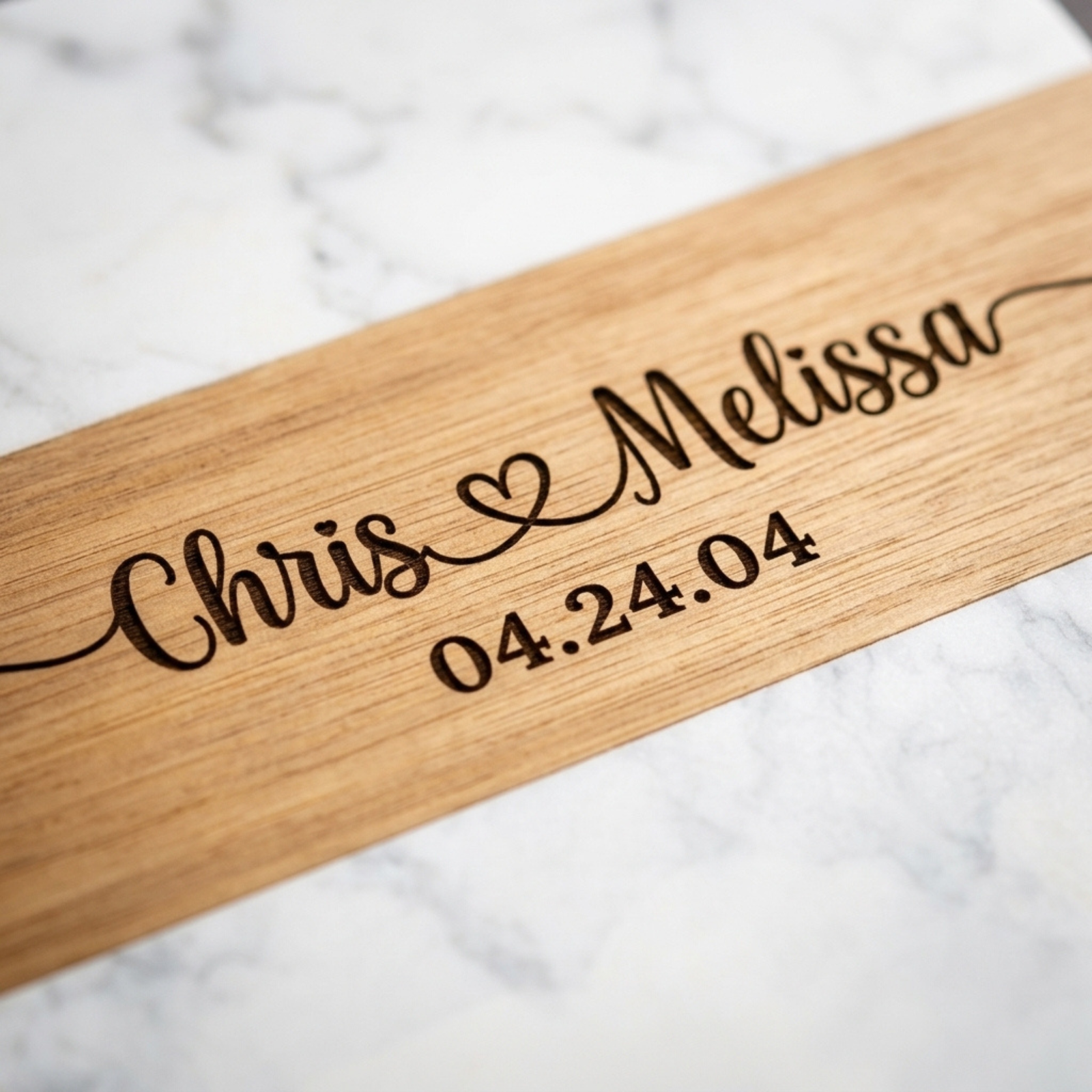 Close view of the acacia center stripe engraved in script with Chris and Melissa joined by a heart and the date 04.24.04 beneath