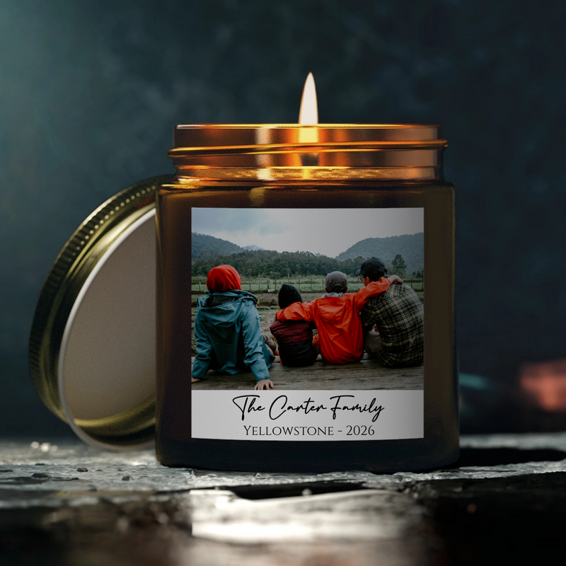 Black glass candle jar with custom photo label showing family at landscape with engraved text sample reading "The Carter Family Yellowstone 2026" and burning wick inside gold lid.