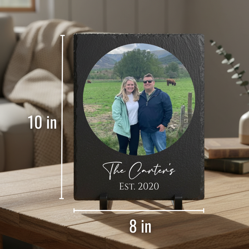 Black slate picture frame with circular photo opening displaying couple in pastoral landscape, engraved with sample text "The Carter's EST. 2020" below the image, shown on easel stand with 10 in height and 8 in width dimensions marked