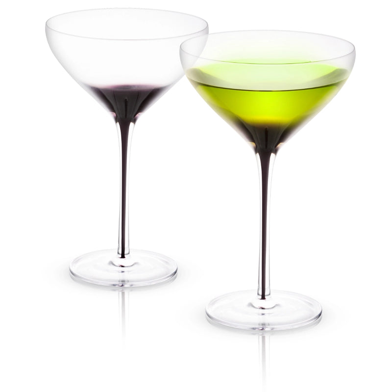 Two crystal martini glasses with black swan-curved stems, one containing red wine and one containing pale green liquid, displayed against white background