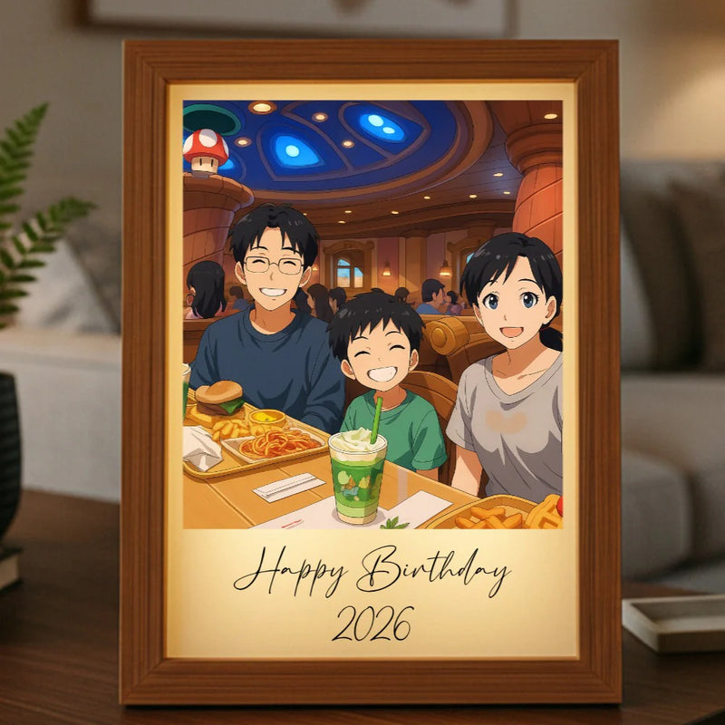 Framed anime-style portrait showing three smiling people dining together, with "Happy Birthday" and "2026" printed below, displayed on a wooden shelf in a home setting.