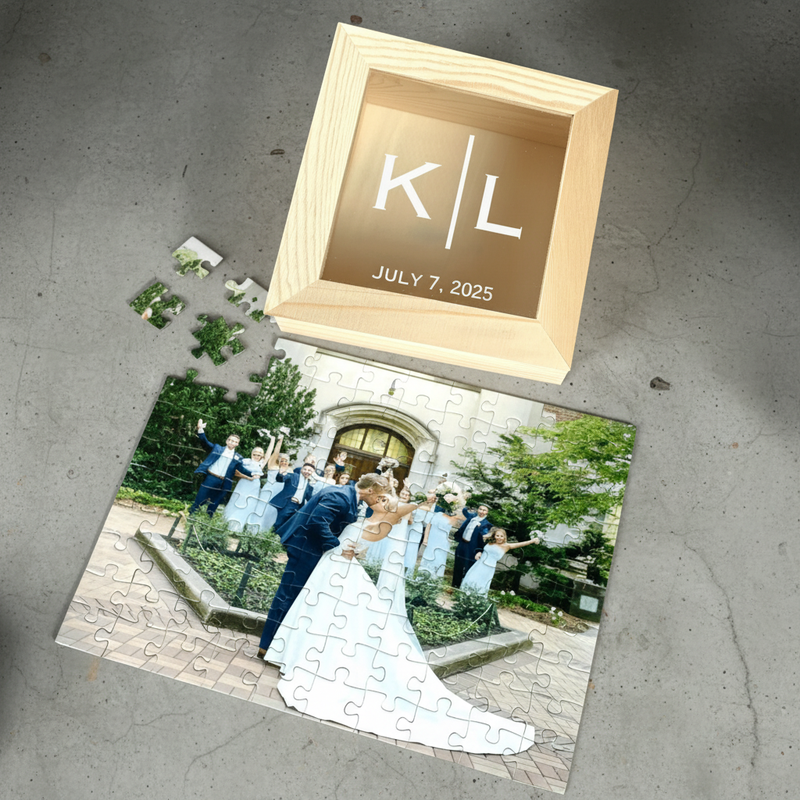 Light wood box with sample initials K and L engraved on tan background and date July 7, 2025, displayed above partially assembled photo puzzle showing wedding couple and guests.