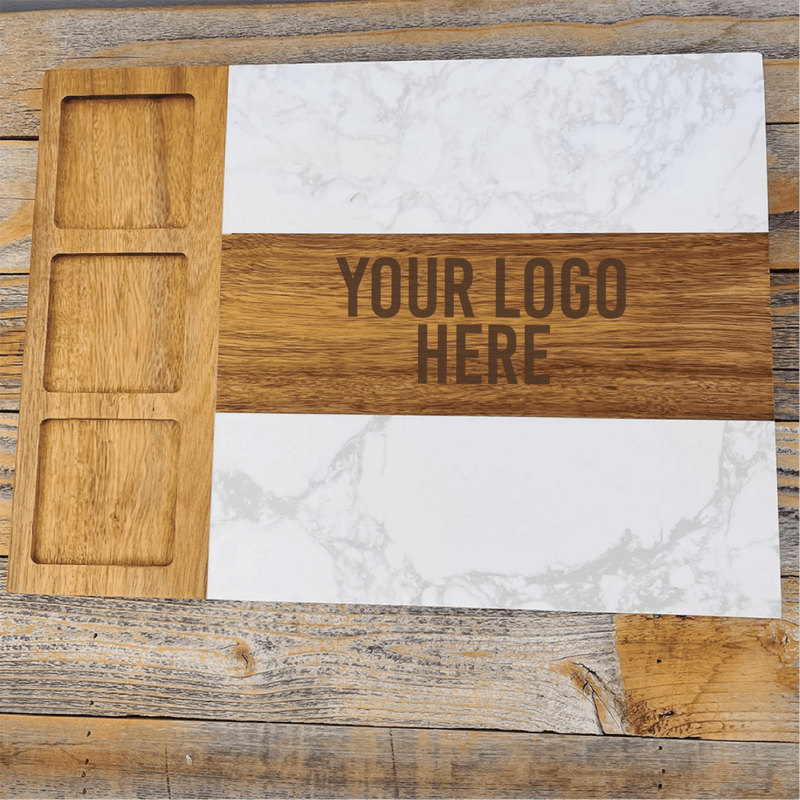Overhead view of wooden charcuterie board with white marble inlay and three recessed bowls on left side, engraved with sample text "YOUR LOGO HERE" on center wood stripe.