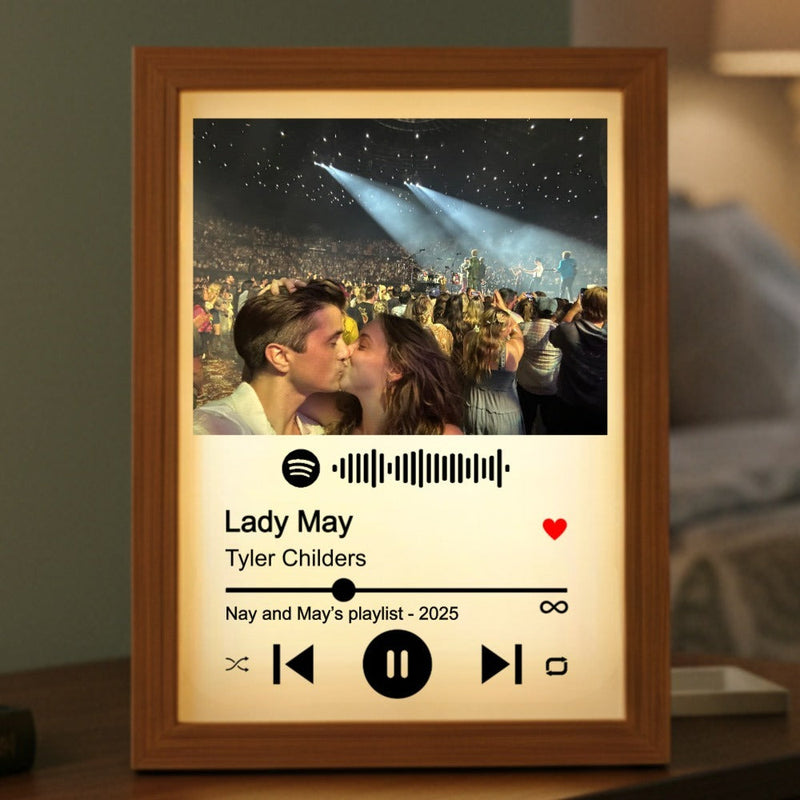 Wooden frame with warm backlight displaying a concert photo, Spotify logo, song title "Lady May" by Tyler Childers, sample text "Nay and May's playlist - 2025", and music player controls with red heart icon