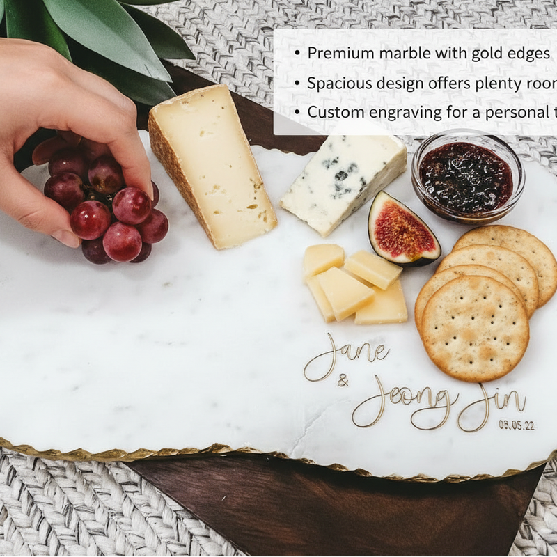 Marble charcuterie board engraved with sample names "Jane & Jeong Jin" and date "03.05.22", styled with cheese, crackers, figs, jam, and grapes.