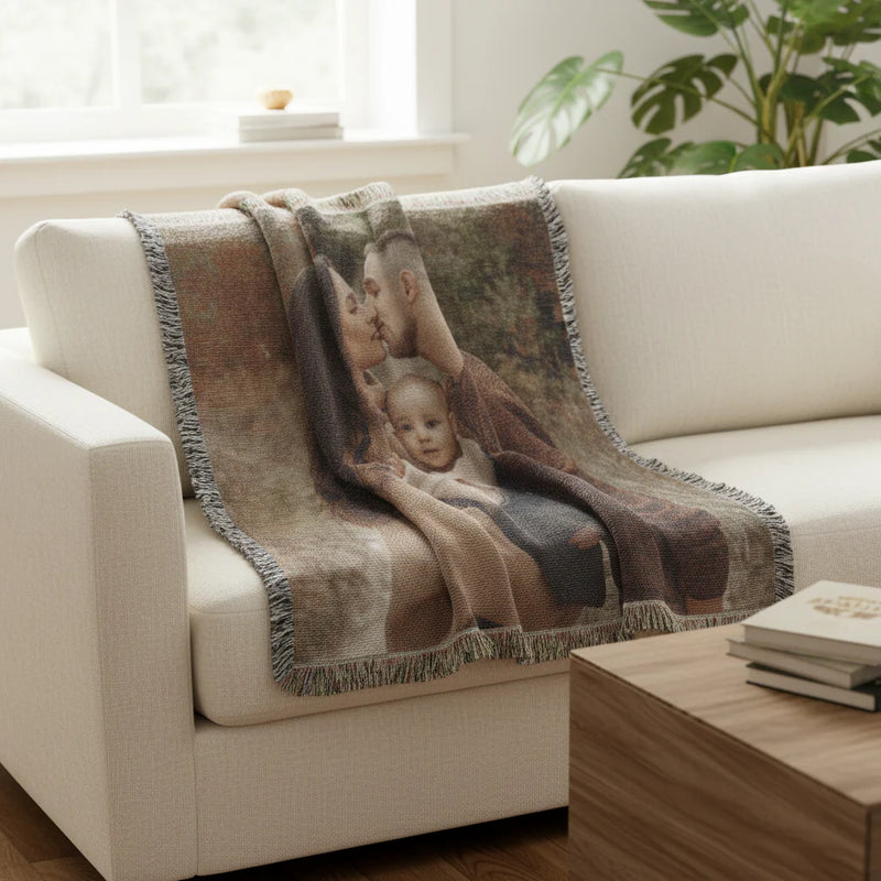 Personalized photo throw blanket draped over cream armchair, displaying woven family portrait with fringe edging in living room setting