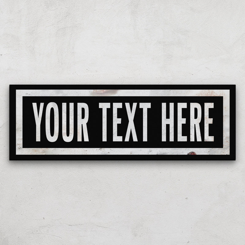 Personalized marquee canvas with sample text "YOUR TEXT HERE" in white lettering on black background with double white border frame, displayed on white textured wall
