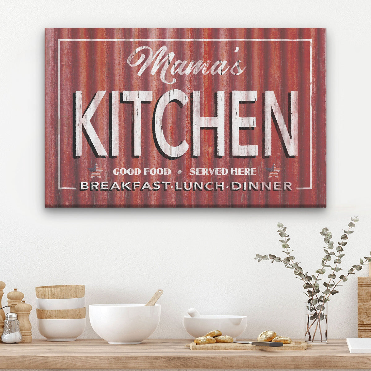 Tin Roof Kitchen Canvas showing "Mama's Kitchen" in bold white lettering above "Good Food · Served Here" and "Breakfast · Lunch · Dinner" on a distressed rust corrugated metal background, mounted above a wooden kitchen counter with white bowls and eucalyptus