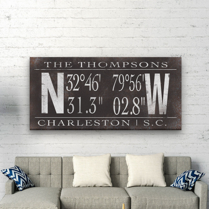 Personalized family coordinates canvas with sample name "THE THOMPSONS" and Charleston, S.C. location coordinates, displayed above a gray sofa with cream pillows