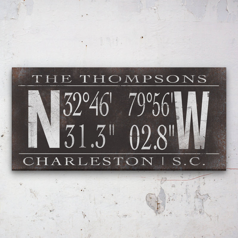 Dark metal-finish canvas with sample personalization showing "THE THOMPSONS" at top, GPS coordinates "32°46' 79°56' / 31.3" 02.8"" in center, and "CHARLESTON | S.C." at bottom, framed by large compass letters N and W
