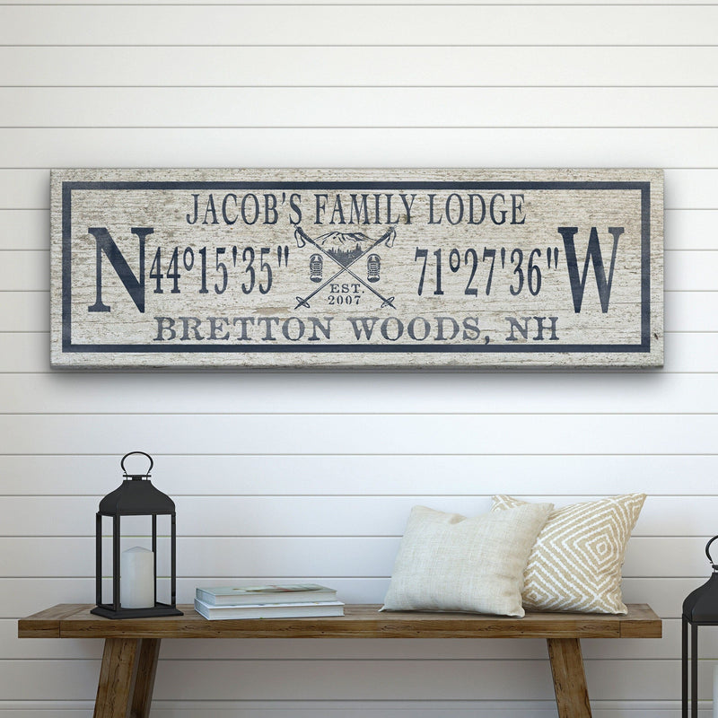 Personalized canvas sign with sample text "Jacob's Family Lodge" and coordinates, displayed on a wooden shelf above white shiplap wall.