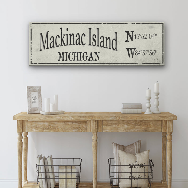 Personalized canvas sign displaying "Mackinac Island" and "Michigan" with GPS coordinates, hung above wooden console table styled with home decor
