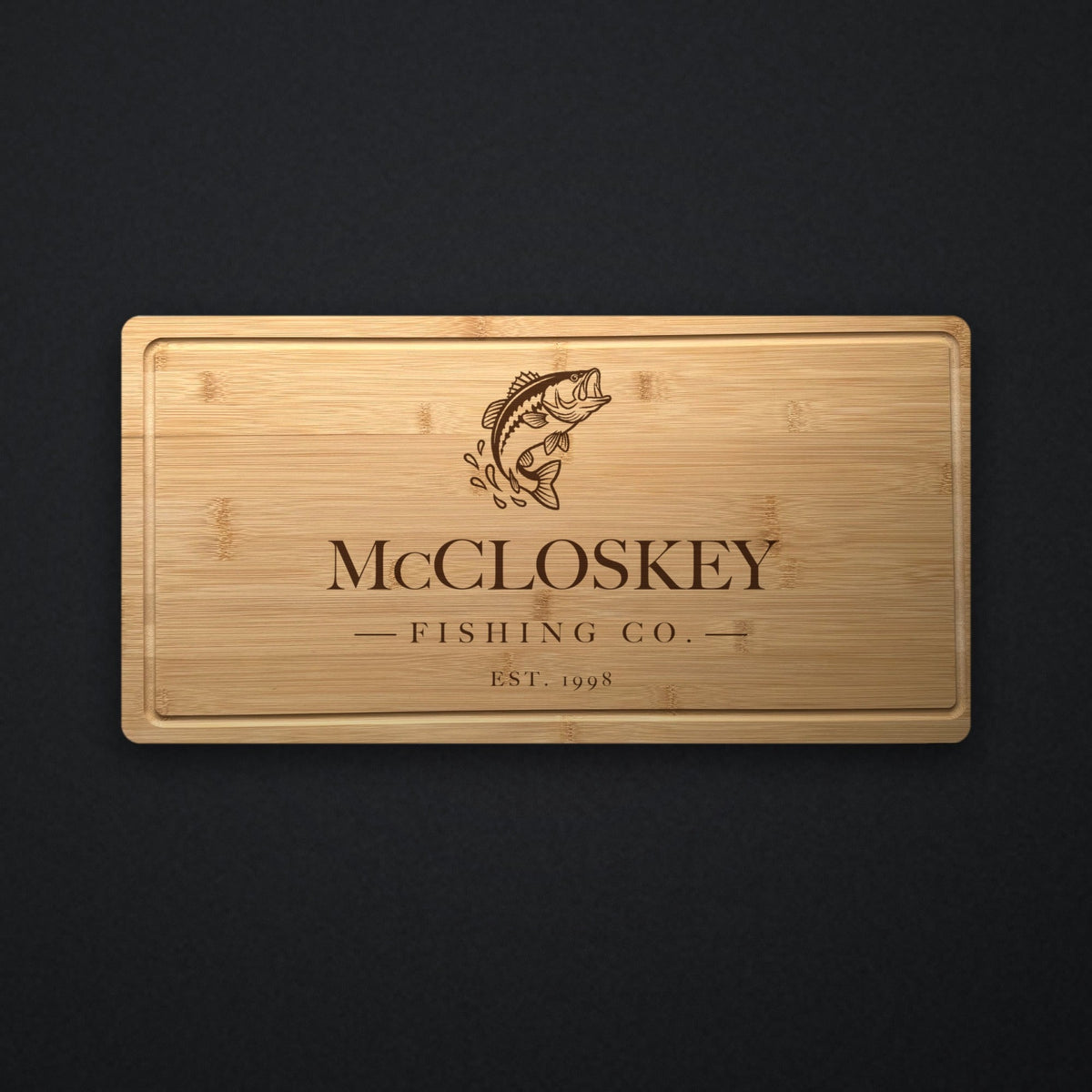 Engraved bass fishing cutting board in solid bamboo showing a leaping bass above a family name, a custom middle line and the established year.