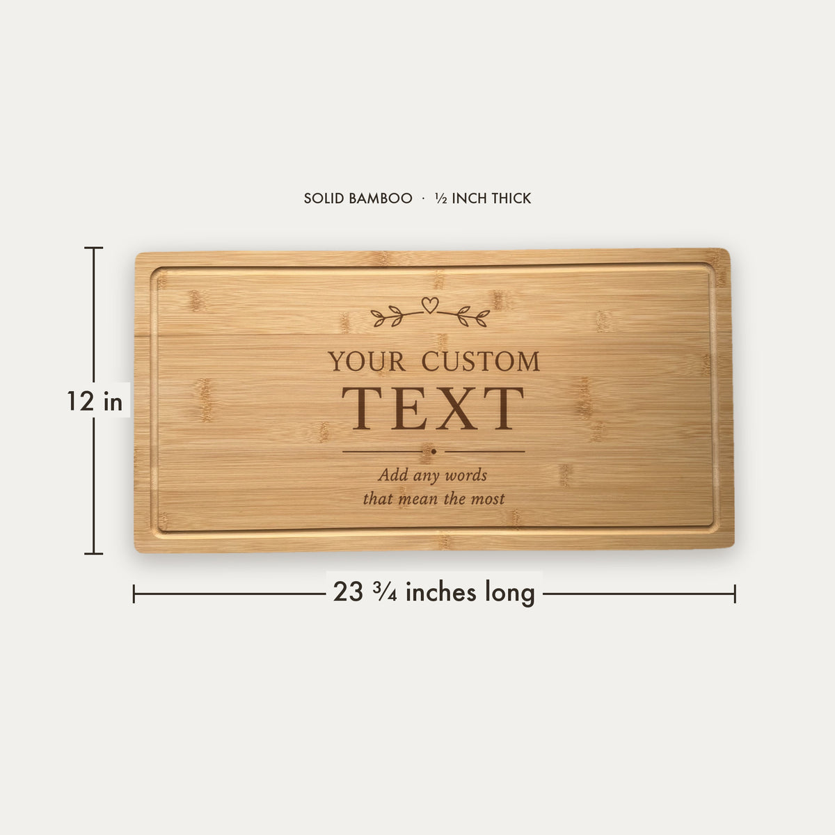 Solid bamboo cutting board with sample engraving showing "YOUR CUSTOM TEXT" centered with decorative heart and leaf motif, 23 3/4 inches long by 12 inches wide