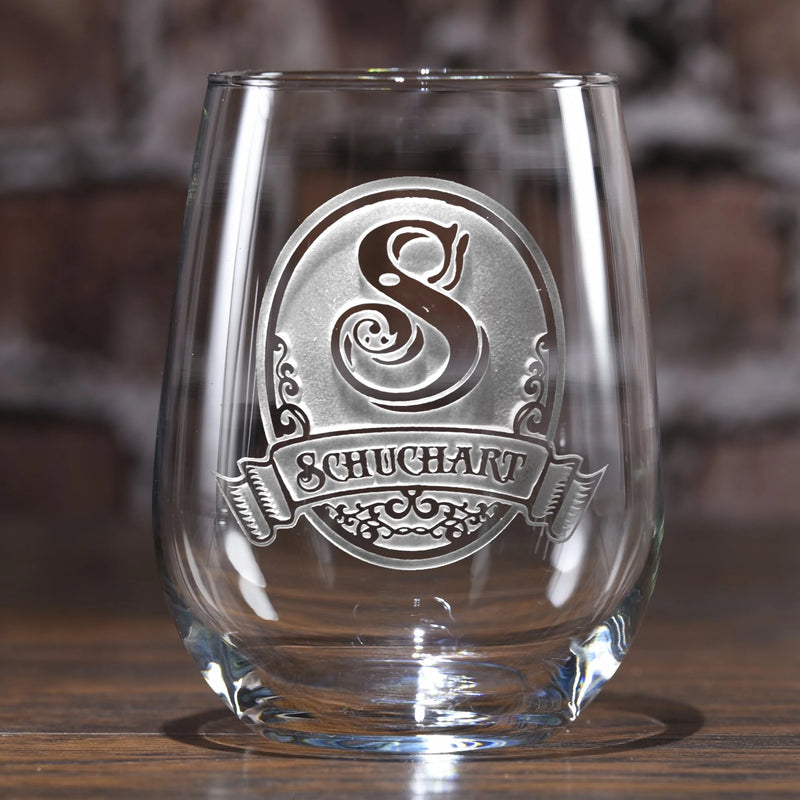 Clear stemless wine glass with sand-carved oval design featuring decorative letter S and "SCHUCHART" banner text, displayed on wooden surface