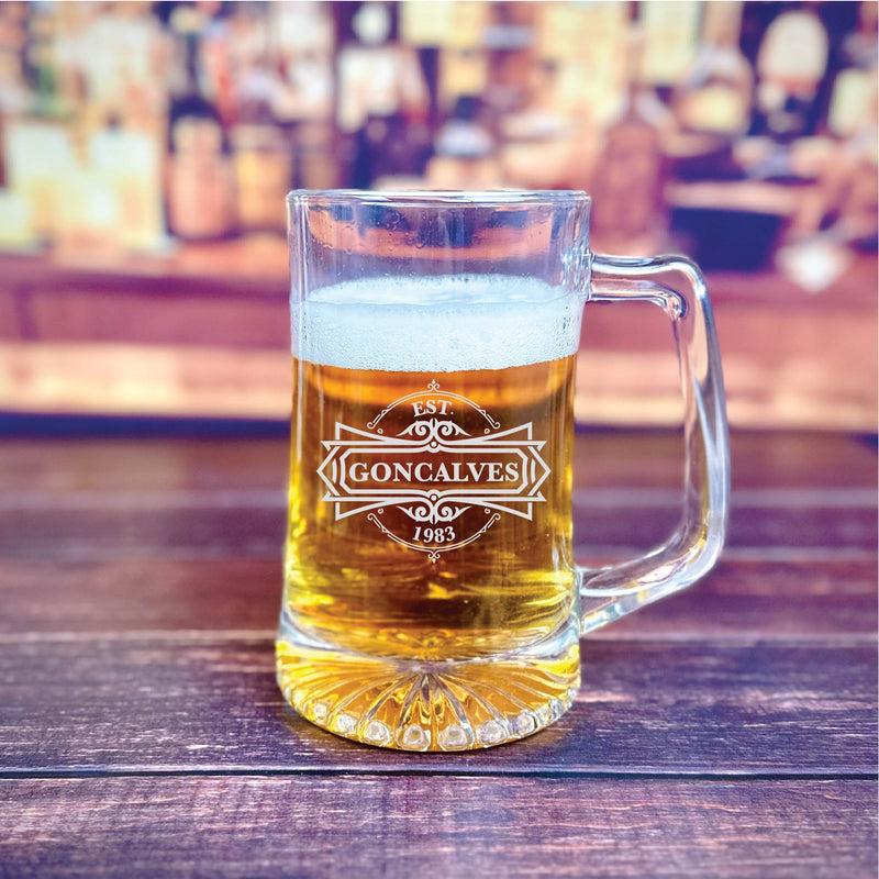 Glass beer mug filled with beer, engraved with "GONCALVES" and "EST. 1983" in decorative white lettering on the front