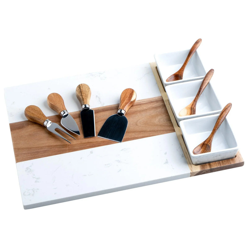 Marble and wood charcuterie board displayed with four cheese knives featuring wooden handles and metal blades, plus four wooden spreaders arranged in white ceramic containers with wooden base