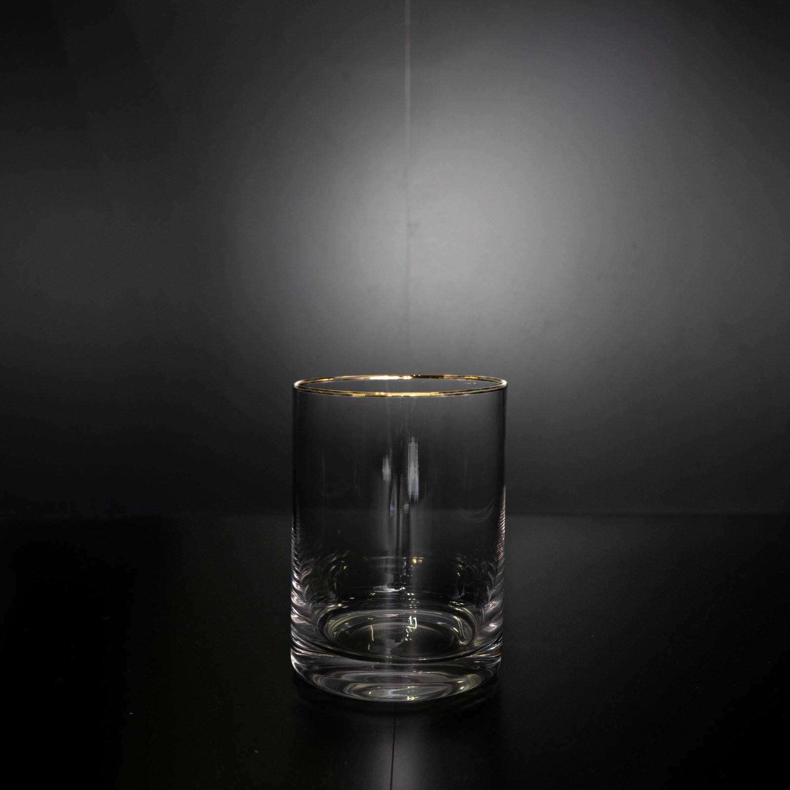 Clear whiskey glass with gold rim and weighted base, shown empty against dark background