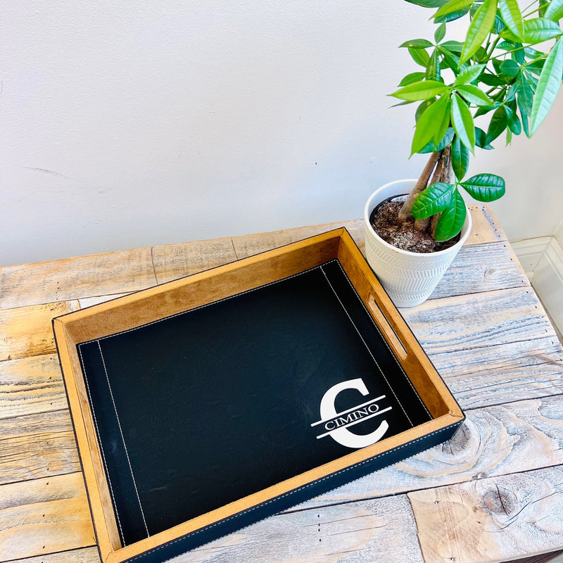 Black leather serving tray with wooden frame displayed on whitewashed wooden table next to potted green plant