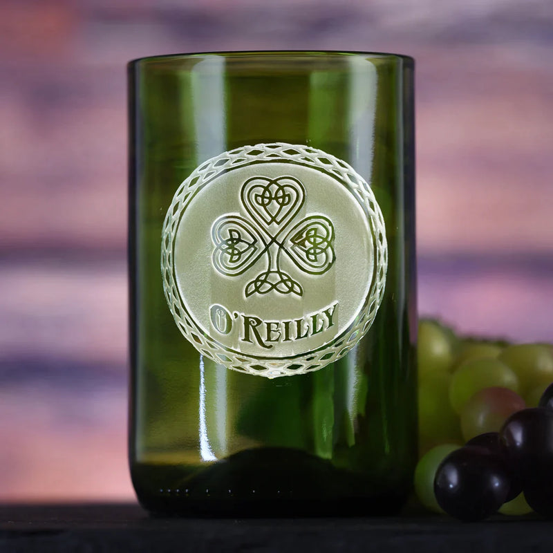 Green recycled wine bottle glass with hand-carved Celtic clover and "O'REILLY" engraved in circular rope-bordered design, displayed against purple background with grapes.