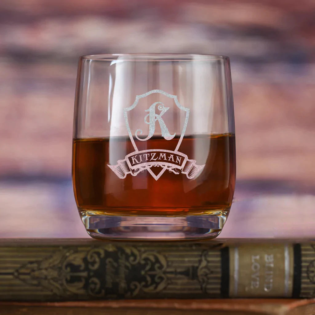 Crystal rocks glass filled with amber liquid, engraved with decorative shield bearing sample name "KITZMAN" and ornamental banner design