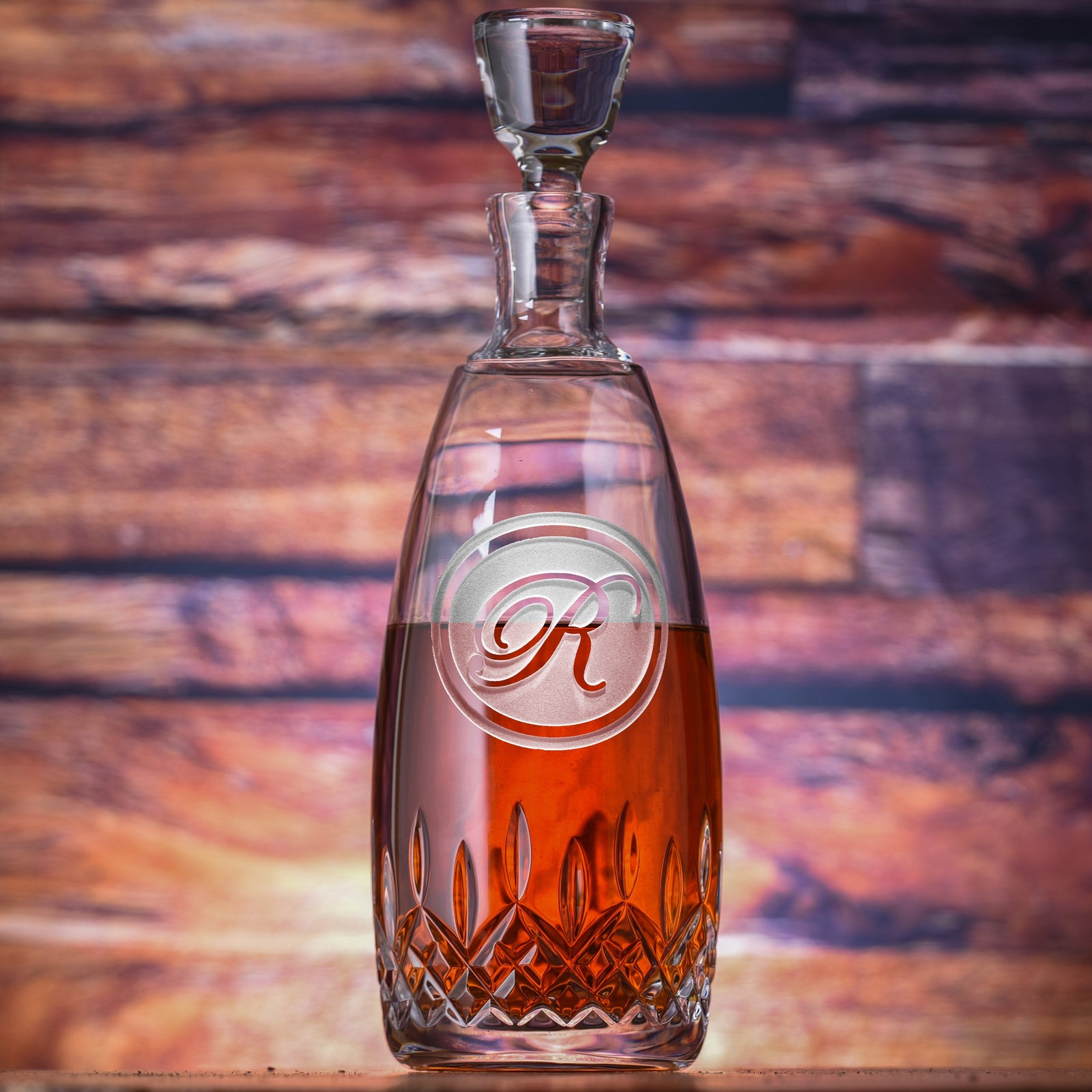 Waterford crystal decanter with cut glass base filled with amber liquid, featuring an engraved circular monogram with sample letter "R" on the front and matching glass stopper