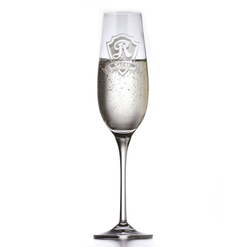 Crystal champagne flute filled with sparkling wine, engraved with decorative shield crest design featuring sample monogram letter "R