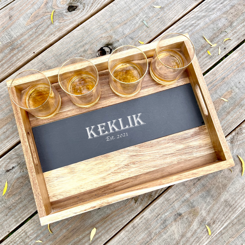 Wooden tray with removable slate insert engraved with sample name "KEKLIK" and "Est. 2021", holding four gold-rimmed whiskey glasses filled with amber liquid