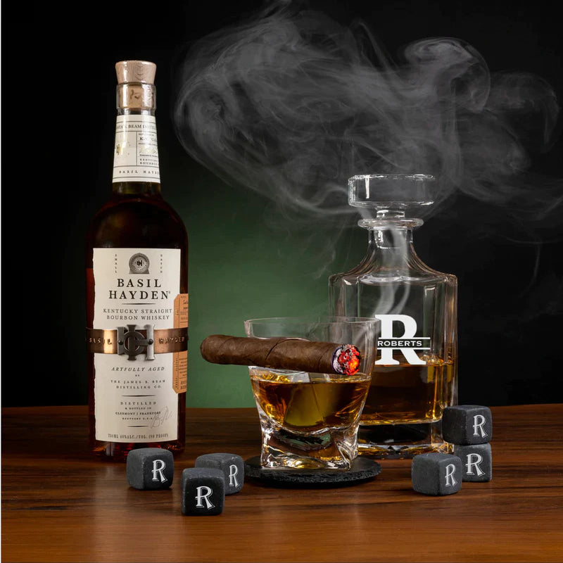 Whiskey decanter and glasses with sample initial "R" engraved on slate whiskey stones and coasters, displayed with bourbon bottle and lit cigar