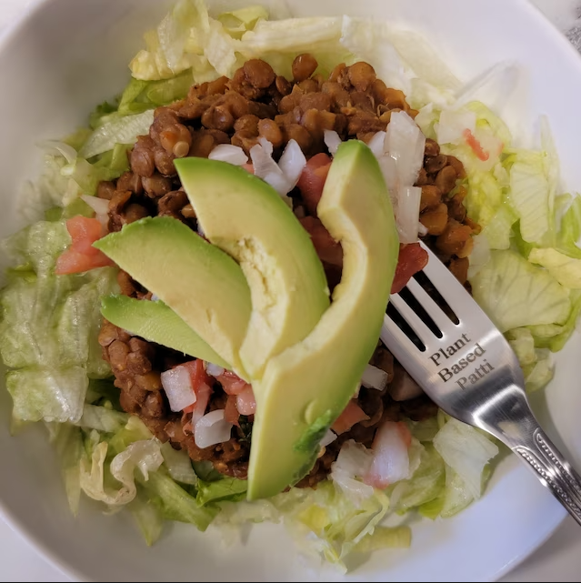 Customized fork with engraved text resting on a plate of salad with seasoned ground meat, avocado slices, and diced onions.