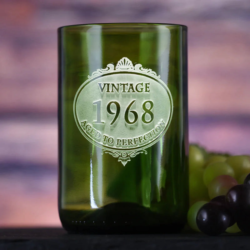 Green wine bottle glass engraved with "Vintage 1968 Aged to Perfection" in decorative medallion design, displayed with grapes in background