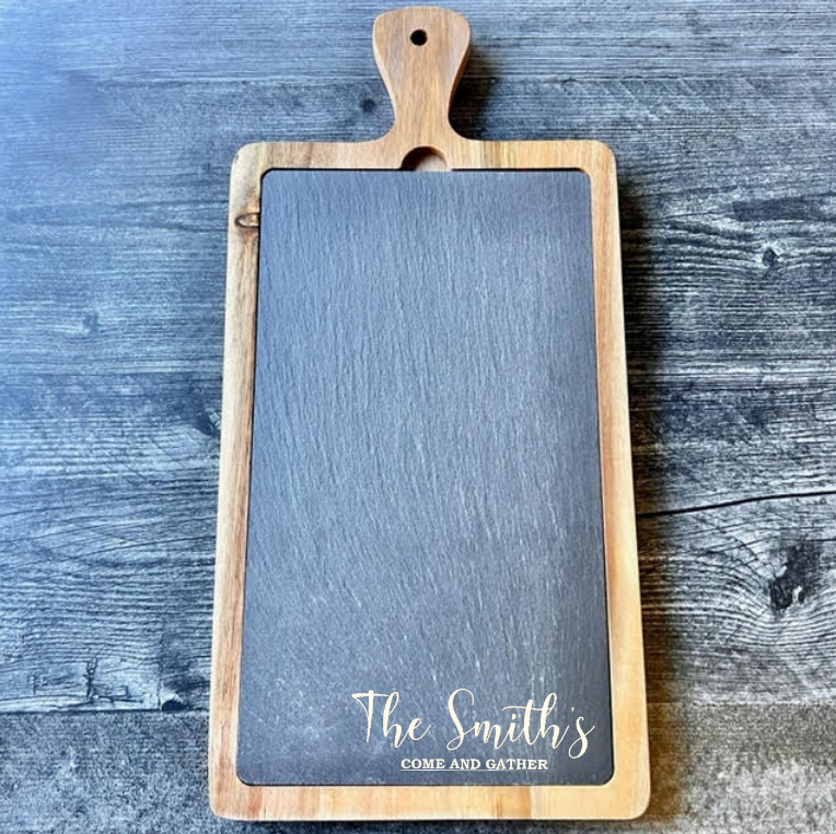Acacia wood and slate serving board with sample engraving reading "The Smith's" and "COME AND GATHER" in gold lettering on the dark slate surface