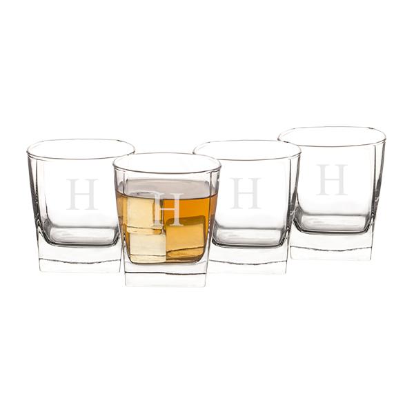 Four whiskey glasses with sample monogram letters engraved on three glasses, one filled with amber liquid and ice