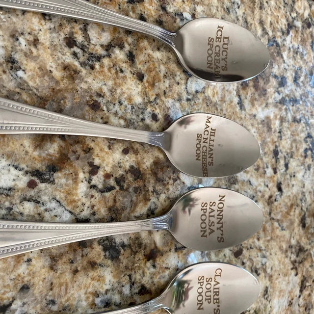 Polished stainless steel spoon with bowl facing up, displayed against weathered wood background, showing reflective surface ready for custom engraving