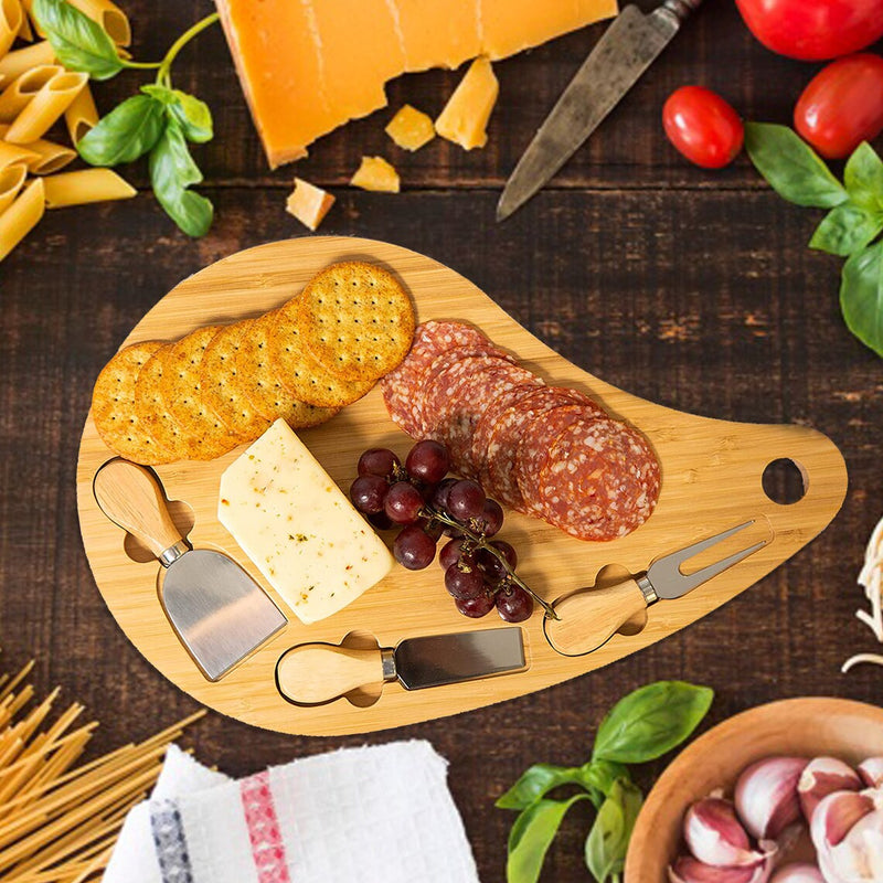 Bamboo teardrop cheese board styled with crackers, sliced salami, cheese wedge, grapes, and three attached serving utensils on dark wooden surface
