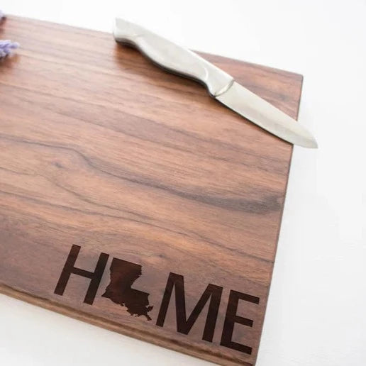 Walnut cutting board with laser-etched "HOME" text and Louisiana state outline, displayed with a white-handled knife on white background