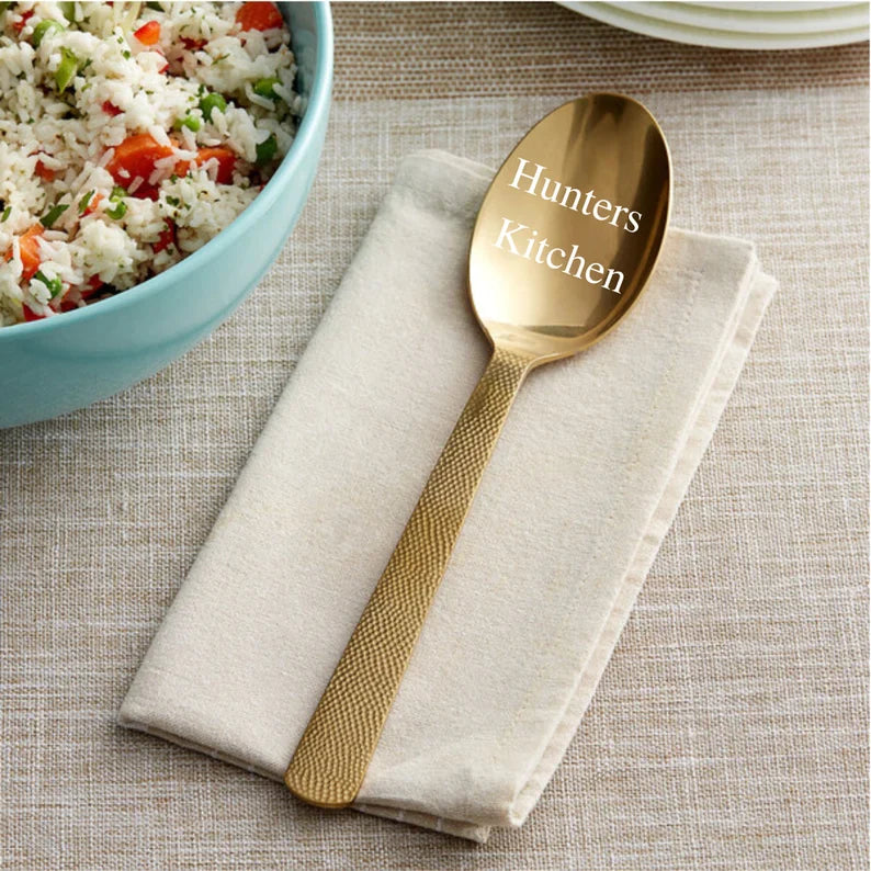 Gold spoon engraved with sample text "Hunters Kitchen" on bowl, resting on cream linen napkin beside turquoise bowl of fried rice