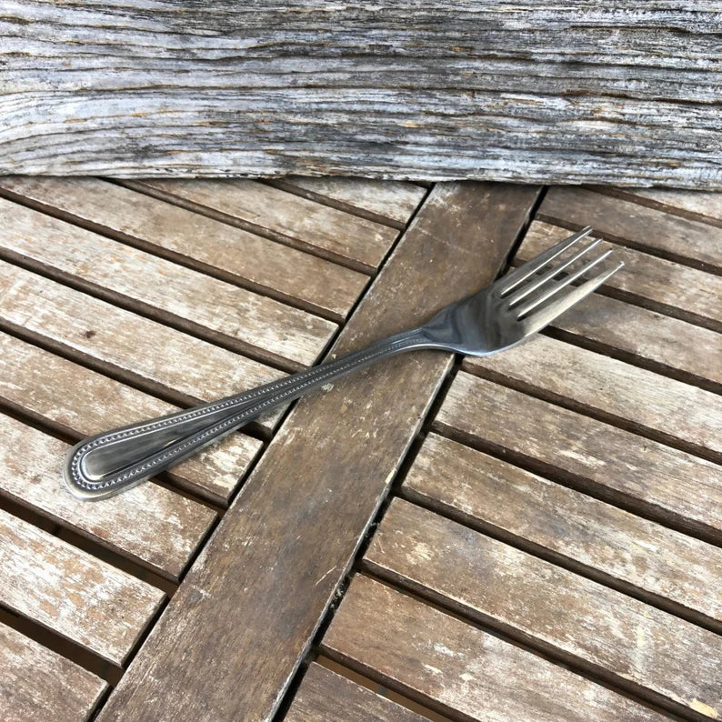 Stainless steel fork engraved with sample text "Custom Engraved Fork" on the handle, displayed on weathered wooden surface