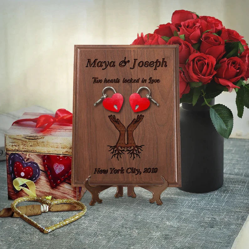 Walnut wood plaque engraved with sample names "Maya & Joseph," decorative tree design, and location "New York City, 2019," displayed with two red heart-shaped padlocks and wooden stand.