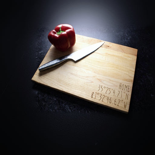 Light maple cutting board with laser-engraved "HOME" text and sample coordinates, styled with red bell pepper and chef's knife on dark surface