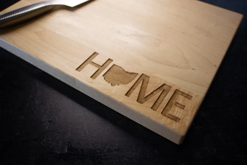 Hardwood cutting board engraved with the word "HOME" and a sample state outline, angled view showing laser-etched detail