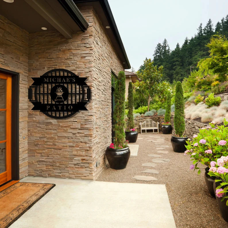 Black metal grill master sign with sample name "MICHAEL'S" mounted on brick patio wall next to orange door