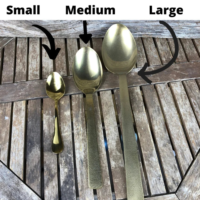 Three gold spoons in small, medium, and large sizes displayed on weathered wood with size labels and directional arrows above each spoon