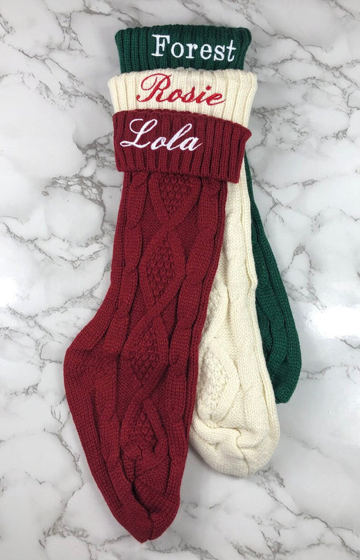 Three embroidered knit Christmas stockings in forest green, cream, and burgundy with sample names "Forest," "Rosie," and "Lola" on the cuffs.