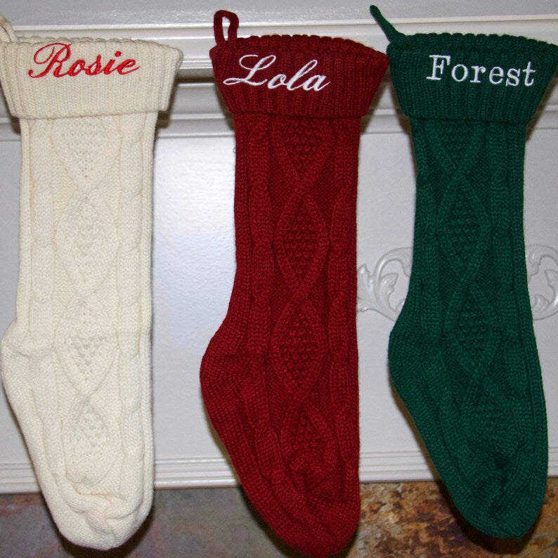 Three knit Christmas stockings in cream, red, and forest green, each embroidered with sample names "Rosie," "Lola," and "Forest" on the cuff