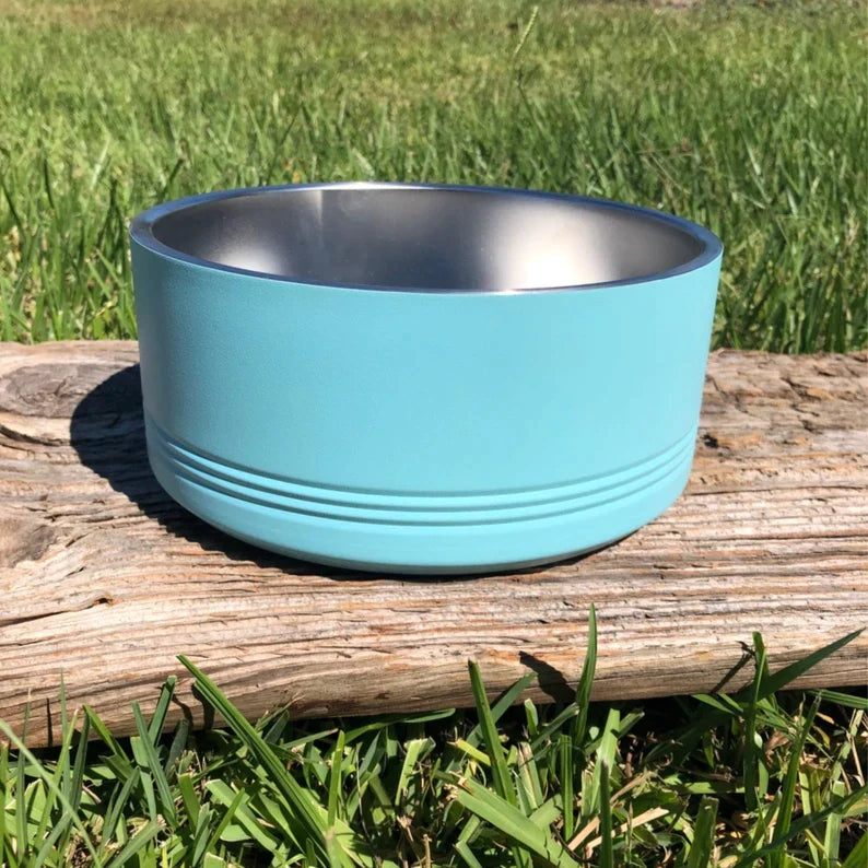 Turquoise dog bowl with stainless steel interior, displayed on weathered wood with grass background