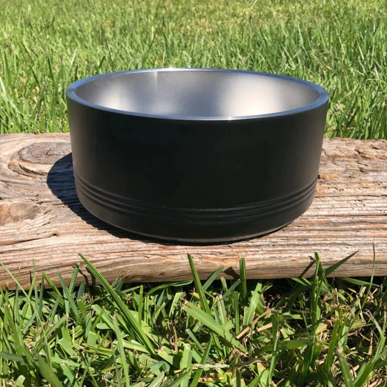 Black stainless-steel dog bowl with brushed interior, displayed on weathered wood outdoors with grass background