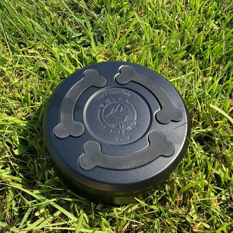 Black dog bowl with molded bone handles shown from above on grass, displaying center medallion with engraved sample dog design and "Hand Wash Only" text