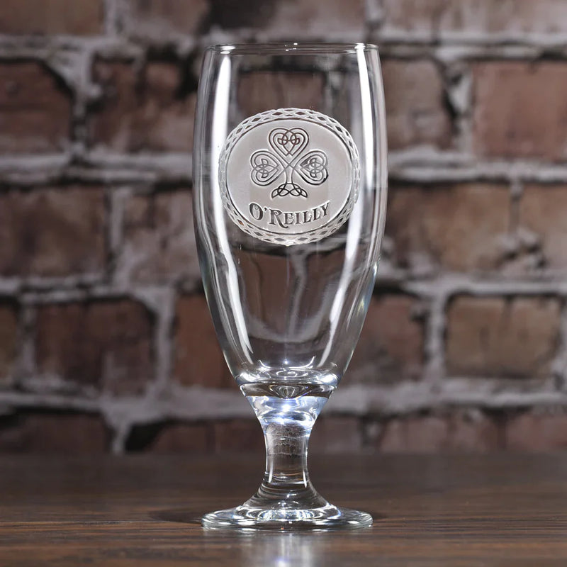 Clear glass goblet with engraved Celtic shamrock design and sample name "O'REILLY" in circular band, displayed against brick background